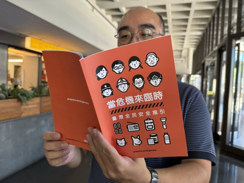 A man holds up a new civil defense handbook meant to provide a more user-friendly revamp highlighting the urgency of strengthening a civilian response in case of an invasion by China in Taipei, Taiwan on Tuesday, Sept. 16, 2025. (AP Photo/Johnson Lai)