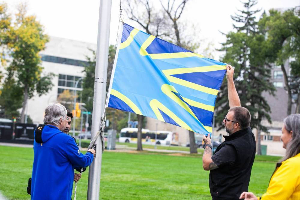 MIKAELA MACKENZIE / FREE PRESS
Manitoba Deaf Association board members Doug Momotiuk (left) and Kayle Miller raise the deaf flag in Memorial Park in front of the Legislative Building on Tuesday.