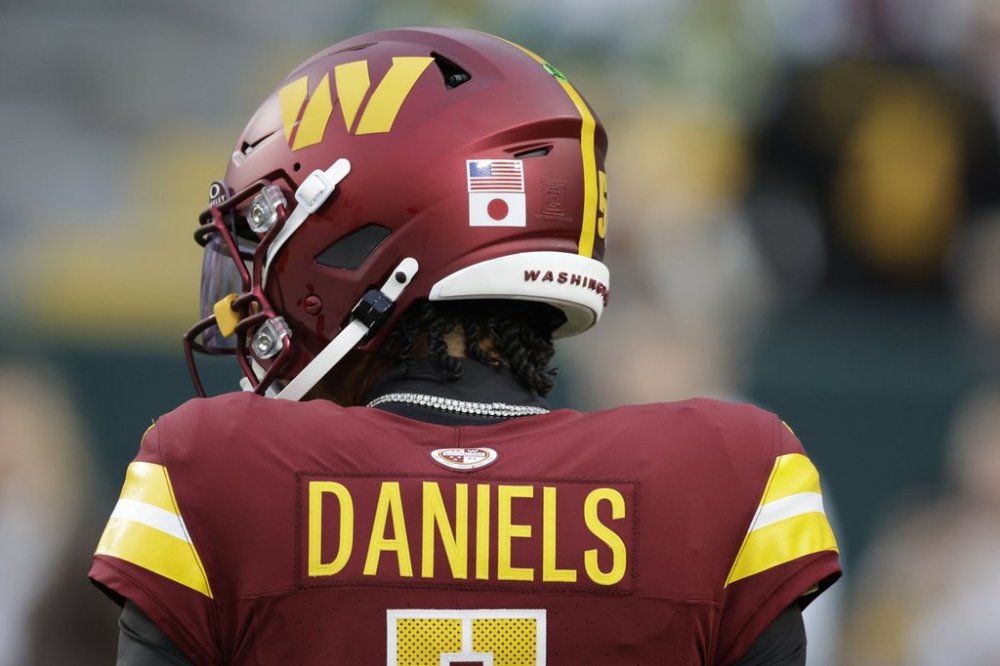 Washington Commanders quarterback Jayden Daniels wears United States and Japan flags on his helmet while warming up before an NFL football game against the Green Bay Packers Thursday, Sept. 11, 2025, in Green Bay, Wis. (AP Photo/Matt Ludtke)