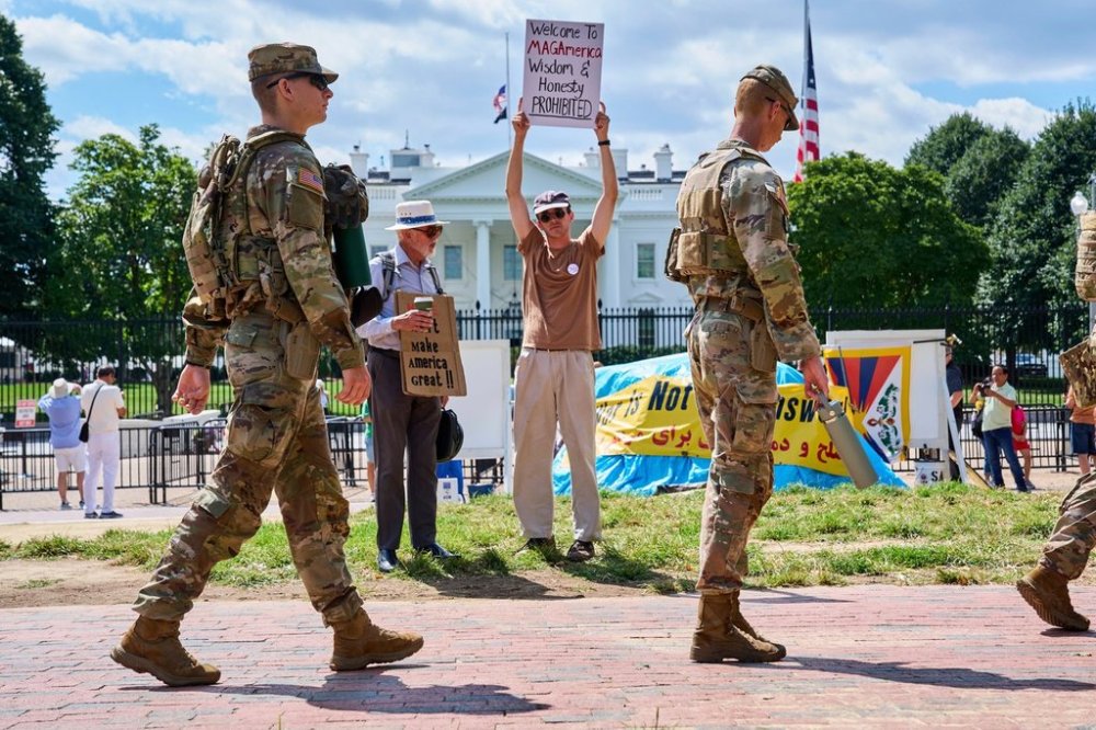 Members of the National Guard patrol Lafayette Park by the White House, Friday, Aug. 29, 2025, in Washington, while protester Will Roosien, of Grand Rapids, Mich., who says he hopes to inspire others of his generation to protest, holds up a sign about the MAGA movement. (AP Photo/Jacquelyn Martin)