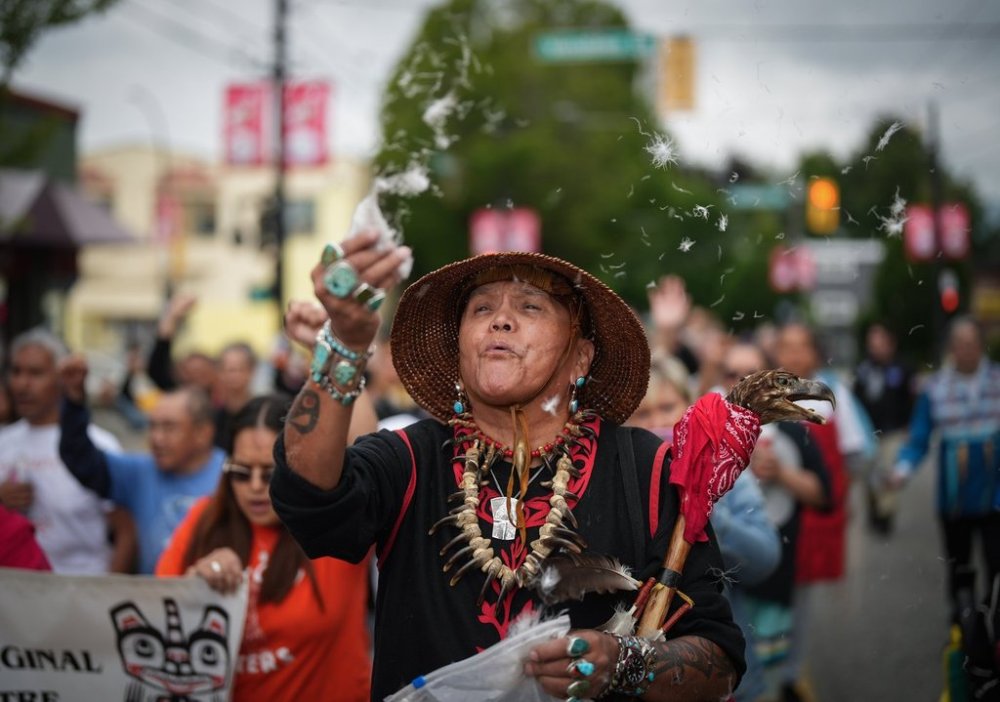 Randy Tait, of the Nisga'a-Gitxsan Nation, blows down feathers into the air during a friendship walk to a National Indigenous Peoples Day gathering, in Vancouver, B.C., Wednesday, June 21, 2023. THE CANADIAN PRESS/Darryl Dyck