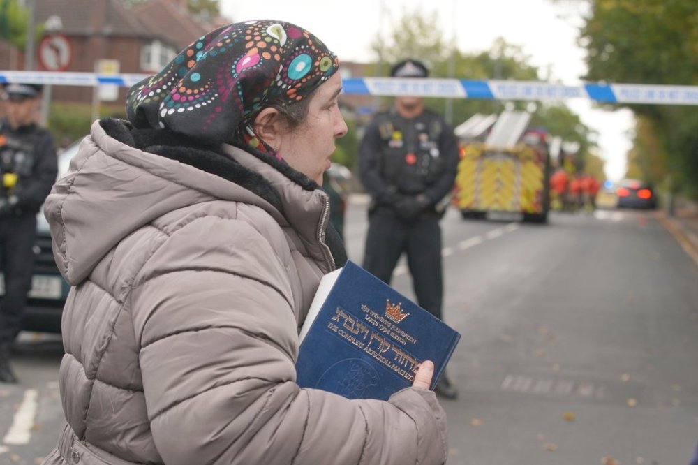 A woman holds a Jewish religious book as she walks near the scene of a stabbing incident at Heaton Park Hebrew Congregation synagogue in Crumpsall, Manchester, England on Thursday, Oct. 2, 2025. (AP Photo/Ian Hodgson)