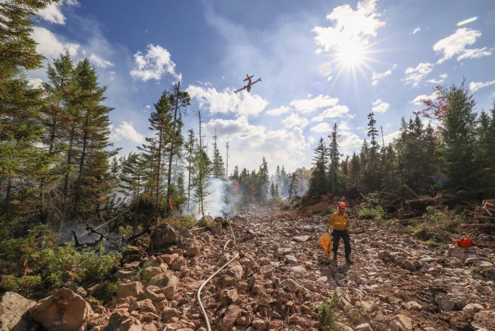 Nova Scotia Department of Natural Resources firefighter Jason Cyr walks on a newly constructed fire break as a water bomber from Newfoundland and Labrador makes a run during firefighting operations on the Lake George wildfire, near Aylesford, N.S., in a Wednesday, Oct. 1, 2025, handout photo. THE CANADIAN PRESS/Handout - Government of Nova Scotia, (Mandatory Credit)