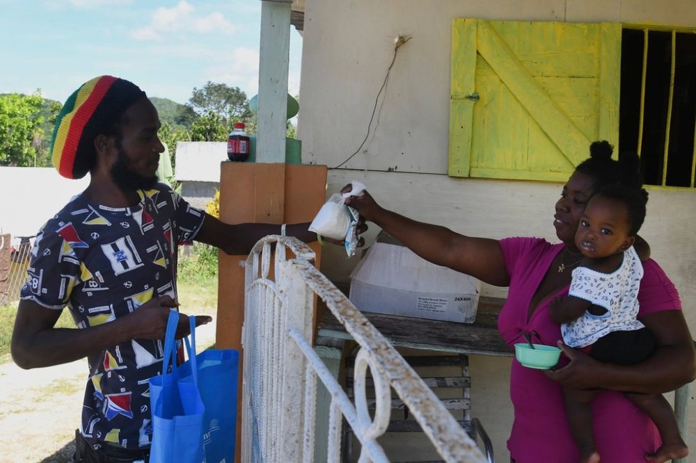 FILE - Gavin James buys a packet of flour from shopkeeper Ann Marie Cawley, in St. Elizabeth, Jamaica, May 17, 2021. (AP Photo/Collin Reid, File)