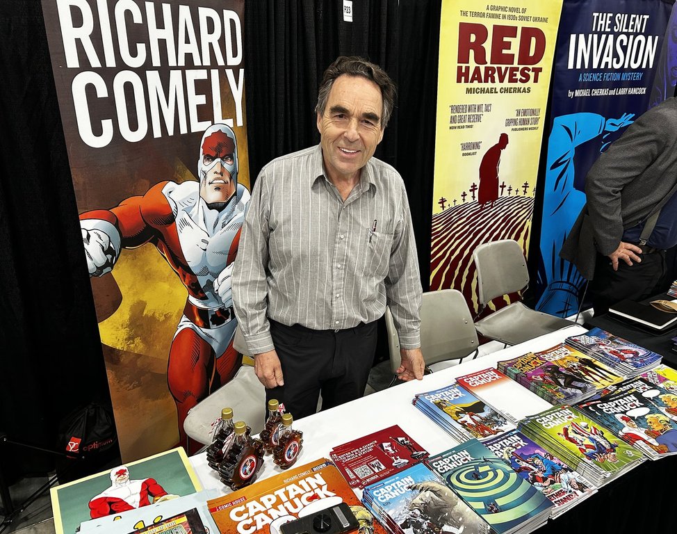 Richard Comely, co-creator of Canadian comic book superhero Captain Canuck, poses with comic books and posters of his character after an interview at the Edmonton EXPO Centre on Friday, Sept. 19, 2025. THE CANADIAN PRESS/Aaron Sousa