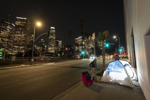 FILE - In this photo illuminated by an off-camera flash, a woman walks past a homeless person's tent with a chair in downtown Los Angeles, Feb. 16, 2023. (AP Photo/Jae C. Hong, File)