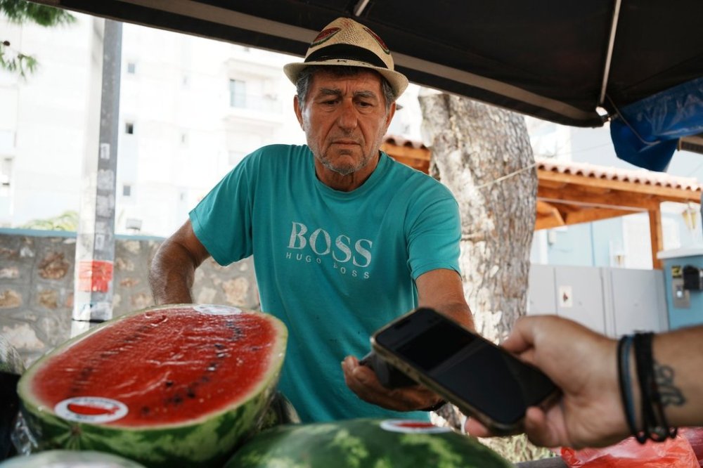 Fruit vendor Makis Panaretos uses a POS terminal for a customer who pays with his cellphone at an open-air fruit and vegetable market in Athens, Greece, Friday, Sept. 5, 2025. (AP Photo/Thanassis Stavrakis)