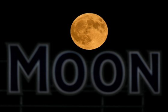 The full moon rises in the over a beer sign in the outfield at Kauffman Stadium in 2024, in Kansas City, Mo. (Charlie Riedel / The Associated Press files)