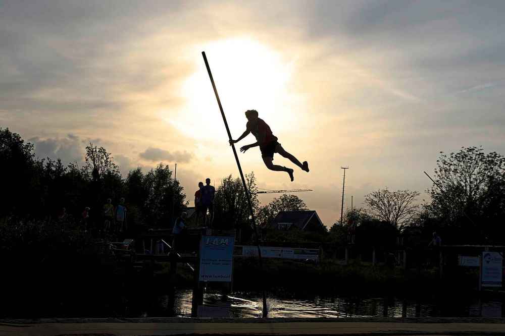 An athlete jumps across a body of water with a long carbon pole during a Fierljeppen competition in Kockengen, Netherlands, Wednesday, Aug. 27, 2025. (AP Photo/Peter Dejong)
