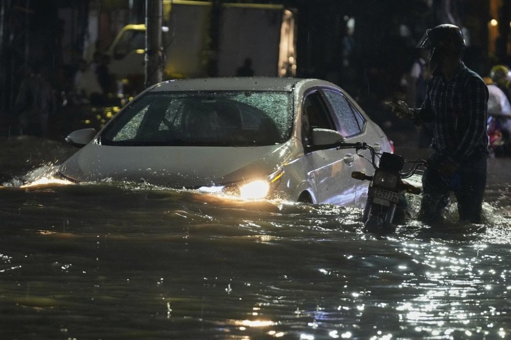 People in car drive and a motorcyclist pushes is vehicle through a flooded road caused by heavy rain in Lahore, Pakistan, Monday, Sept. 8, 2025. (AP Photo/K.M. Chaudary)