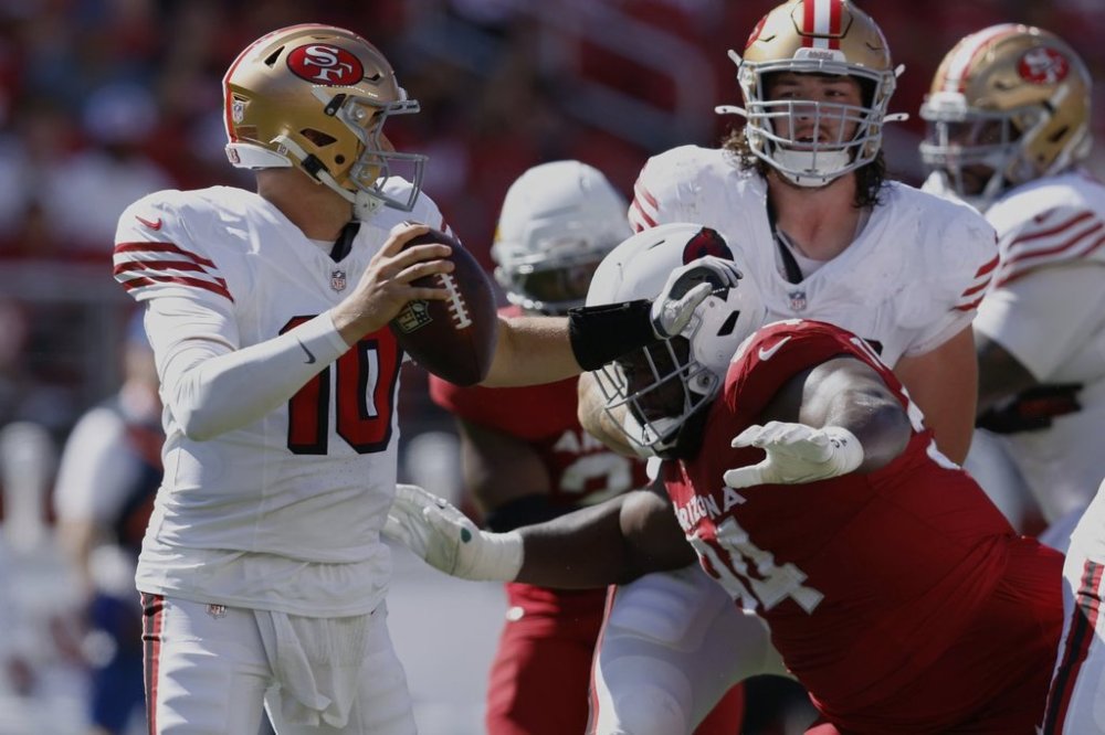 San Francisco 49ers quarterback Mac Jones, left, avoids a tackle by Arizona Cardinals defensive end Dalvin Tomlinson during the second half of an NFL football game Sunday, Sept. 21, 2025, in Santa Clara, Calif. (AP Photo/Sergio Estrada)