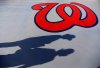 FILE - Fans cast shadows past a Washington Nationals logo as they walk in to Space Coast Stadium for an exhibition spring training baseball game between the Nationals and the New York Mets, Thursday, March 5, 2015, in Viera, Fla. (AP Photo/David Goldman, File)