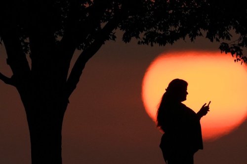 FILE - A woman looks at her phone while watching the sun set in Kansas City, Mo., on Aug. 20, 2023. (AP Photo/Charlie Riedel, File)