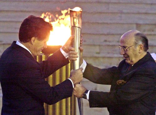 FILE - Lambis Nikolaou, head of the Greek Olympic Committee, right, hands the Olympic Flame to Mitt Romney, head of the Salt Lake Organizing Committee, at the Panathenian stadium in Athens on Dec. 3, 2001. (AP Photo/Thanassis Stavrakis, file)
