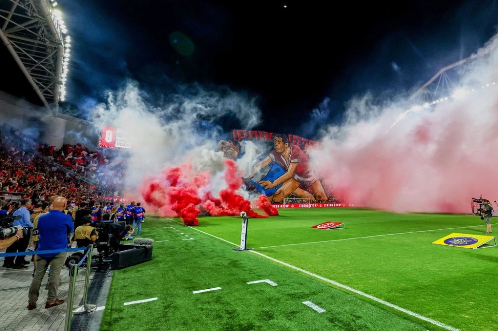 Smoke from flares thrown by fans fills the field before the soccer derby between Maccabi Tel Aviv and Hapoel Tel Aviv was called off Sunday after pregame disturbances led police to deem it unsafe to proceed at Bloomfield Stadium in Tel Aviv, Israel, Sunday, Oct. 19, 2025 . (AP Photo/Nir Keidar)