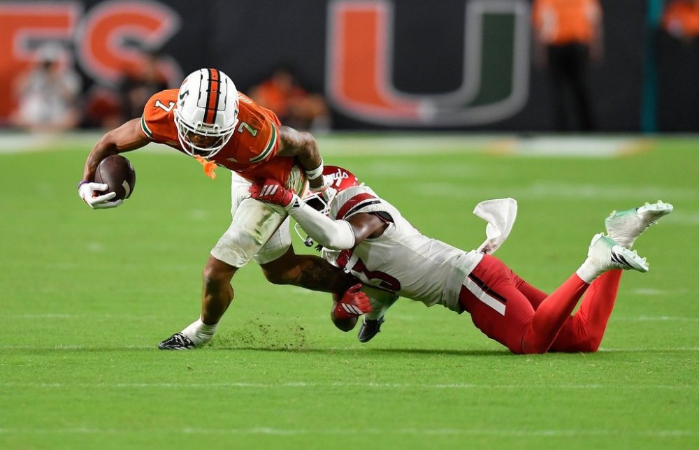 Miami wide receiver CJ Daniels (7) is tackled by Louisville cornerback Justin Agu during the second half of an NCAA college football game, Friday, Oct. 17, 2025, in Miami Gardens, Fla. (AP Photo/Michael Laughlin)