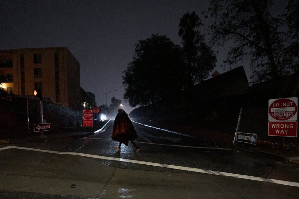 A homeless person walks under gusty showers in East Los Angeles early morning Tuesday, Oct. 14, 2025. (AP Photo/Damian Dovarganes)