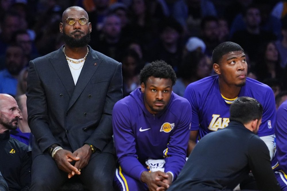 Los Angeles Lakers forward Lebron James, left, guard Bronny James, center, and forward Rui Hachimura (28) watch from the bench during the first half of an NBA basketball game against the Los Angeles Lakers, Tuesday, Oct. 21, 2025, in Los Angeles. (AP Photo/Ethan Swope)