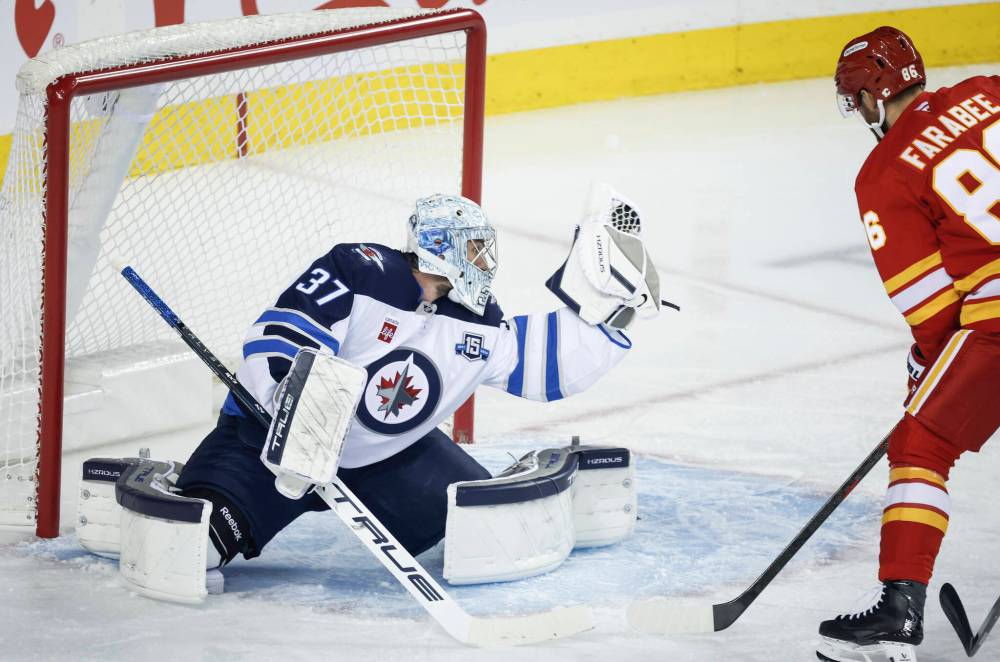 Jeff McIntosh / THE CANADIAN PRESS
Winnipeg Jets goalie Connor Hellebuyck, left, makes one of his 32 saves against the Calgary Flames as Joel Farabee looks on in the first period in Calgary, Monday.