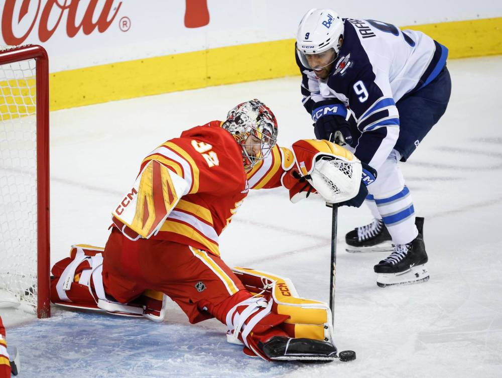 Jeff McIntosh / THE CANADIAN PRESS
Jets forward Alex Iafallo (right) tries to poke the puck past Flames goalie Dustin Wolf on Monday night in Calgary.