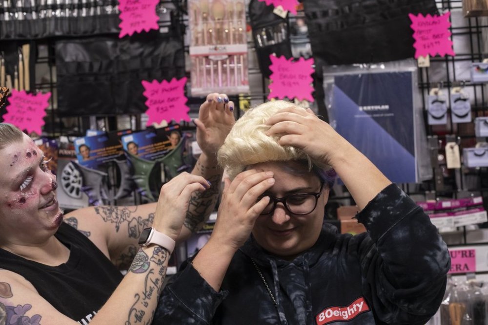 Stephanie LaBute tries on a Donald Trump style of wig, wth the help of Tori Larson at Theatre Garage in Edmonton on Friday, October 24, 2025.  THE CANADIAN PRESS/Amber Bracken