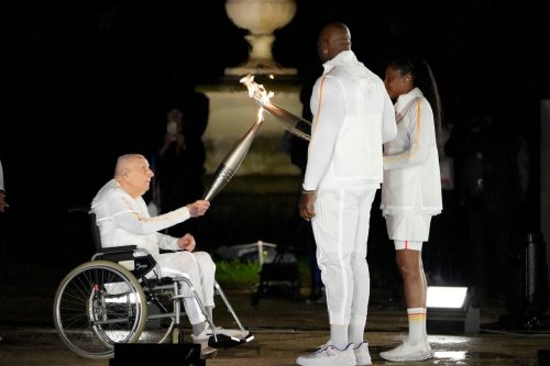 FILE - Charles Coste, left, passes the flame to Teddy Riner and Marie-Jose Perec in Paris, France, during the opening ceremony of the 2024 Summer Olympics, Friday, July 26, 2024. (AP Photo/David Goldman, File)