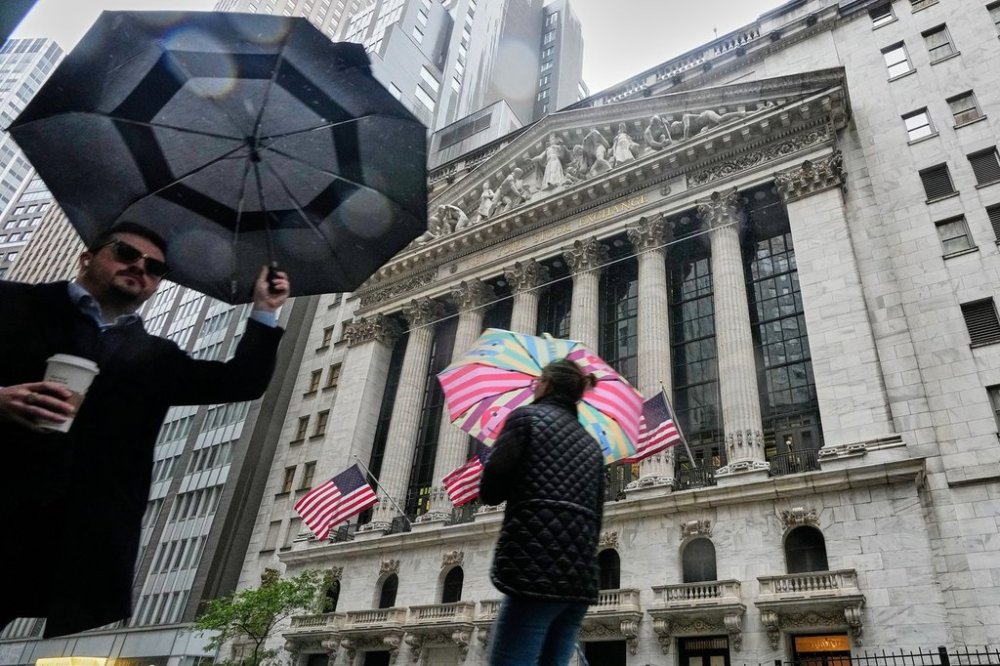 People with umbrellas pass the New York Stock Exchange, Monday, Oct. 13, 2025. (AP Photo/Richard Drew)