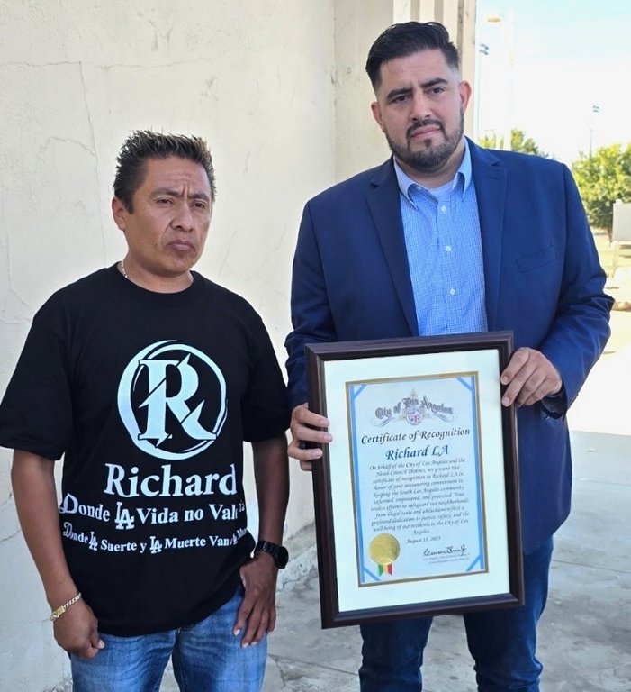 In this photo provided by the office of Los Angeles City Councilmember Curren Price, Carlitos Ricardo Parias, left receives a certificate of recognition from Jose Ugarte, chief of staff for Los Angeles City Councilmember Curren Price in Los Angeles, Aug. 2025. (Office of Los Angeles City Councilmember Curren Price via AP)