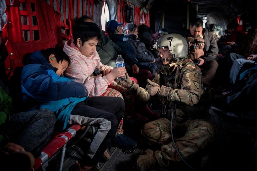In this photo provided by the Alaska Army National, Guard Sgt. Mary Miller, a helicopter crew chief, passes a bottle of water to a child while evacuating displaced people from Kwigillingok, Alaska, during recovery operations on Thursday, Oct. 16, 2025. (Joseph Moon/Alaska National Guard via AP)