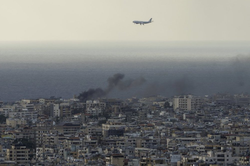A Middle East Airlines airplane flies over Beirut as smoke rises from Israeli airstrikes in Dahiyeh, Beirut on Tuesday, Oct. 1, 2024. (AP Photo/Bilal Hussein)