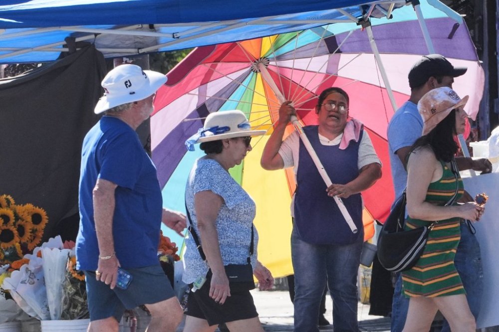 A street vendor uses an umbrella to shelter from the sun on a unseasonably hot day Tuesday, Oct. 28, 2025, in Los Angeles. (AP Photo/Damian Dovarganes)