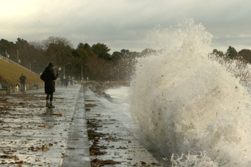 People walk along a sidewalk as waves and debris crash into the breakwater below Dallas Rd. in Victoria, B.C., on Wednesday, Nov. 20, 2024. Severe weather conditions overnight caused power outages across Vancouver Island. THE CANADIAN PRESS/Chad Hipolito