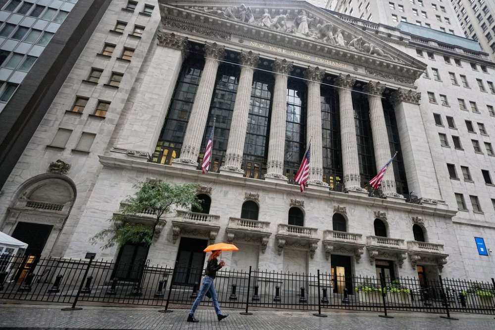 A woman with an umbrella passes the New York Stock Exchange, Monday, Oct. 13, 2025. (AP Photo/Richard Drew)