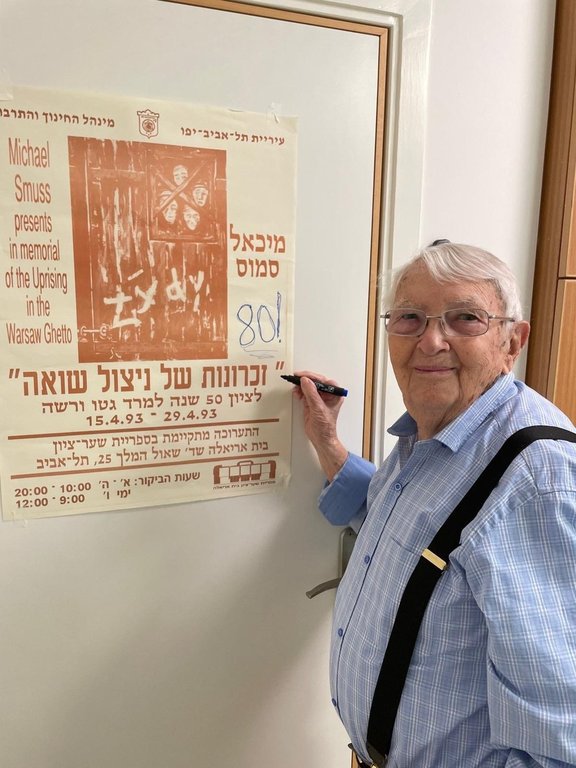 This undated handout photo, courtesy of Michael Smuss’ family, shows Michael Smuss holding a marker next to a placard commemorating the 50 anniversary of the Warsaw Ghetto Uprising. (Michael Smuss’ family via AP)