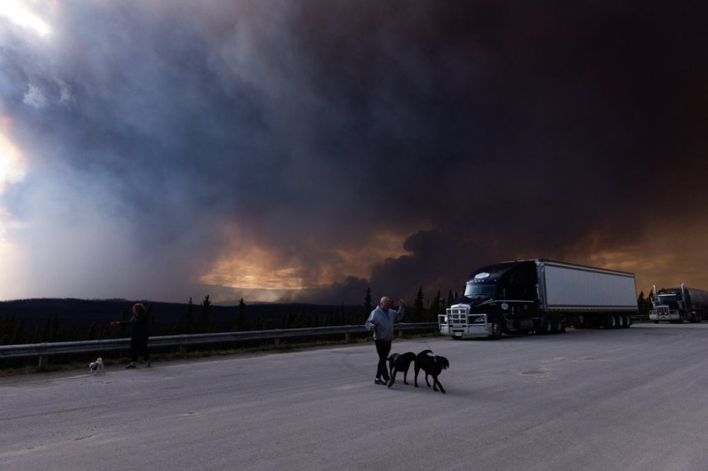 People take their dogs out for a quick break under billowing wildfire smoke off Highway 97 north of Buckinghorse River, B.C. on Friday, May 30, 2025. THE CANADIAN PRESS/Nasuna Stuart-Ulin