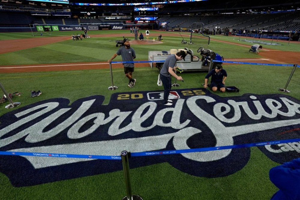 Blue Jays grounds crew members Coleton Miller, centre, and Jake Matthew, right, work on the World Series logo during a baseball media day on Oct. 23, 2025, in Toronto. The Toronto Blue Jays face the Los Angeles Dodgers in Game 1 on Friday. (AP Photo/David J. Phillip)