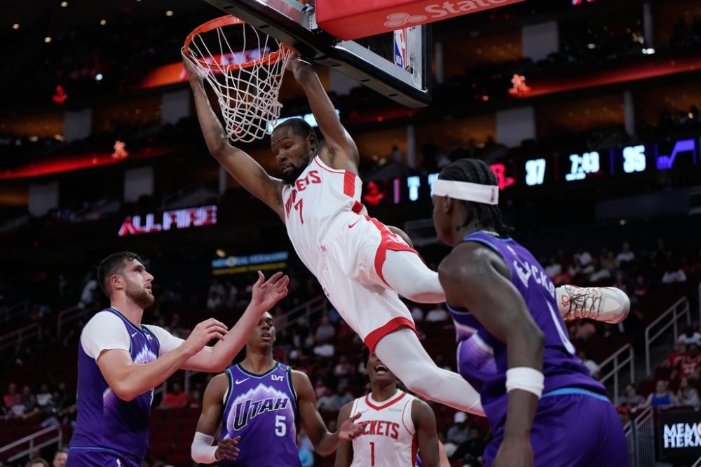 Houston Rockets forward Kevin Durant (7) hangs from the hoop after dunking during the first half of an NBA basketball preseason game against the Utah Jazz in Houston, Wednesday, Oct. 8, 2025. (AP Photo/Ashley Landis)