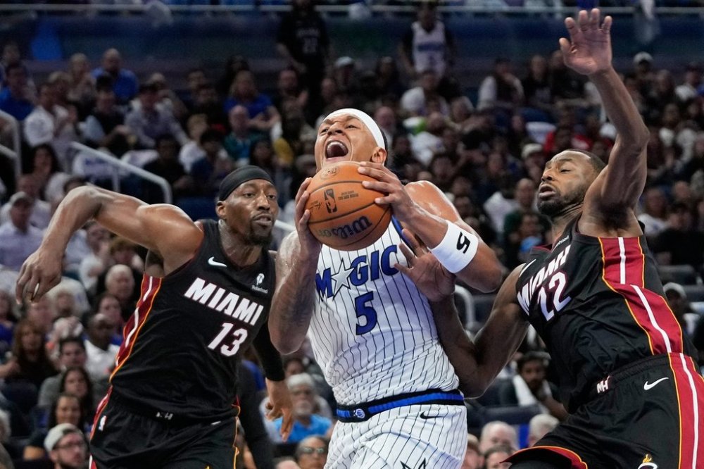 Orlando Magic forward Paolo Banchero (5) gets off a shot as he moves betweernMiami Heat center Bam Adebayo (13) and forward Andrew Wiggins (22) during the second half of an NBA basketball game, Wednesday, Oct. 22, 2025, in Orlando, Fla. (AP Photo/John Raoux)