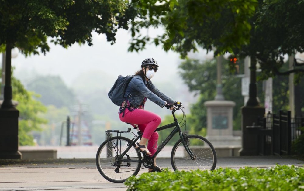A person wears a mask as they cycle through Majors Hill park in Ottawa on Friday, June 6, 2025, as forest fire smoke from Manitoba hangs over the National Capital region. THE CANADIAN PRESS/Sean Kilpatrick