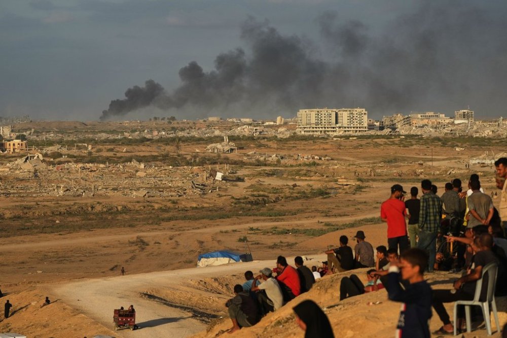 Displaced Palestinians watch smoke rise after Israeli military strikes as they gather on the coastal road near Wadi Gaza, in the central Gaza Strip, Thursday, Oct. 9, 2025. (AP Photo/Abdel Kareem Hana)