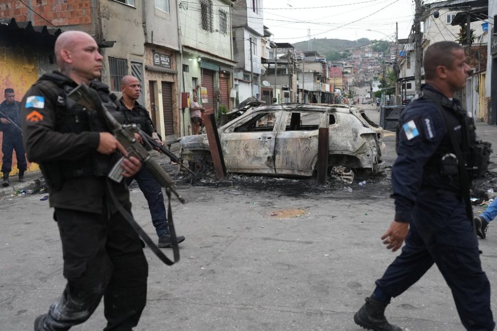 Police walk past a burned car used by alleged drug traffickers as a roadblock during a police operation in the Complexo do Alemao favela where the criminal organization