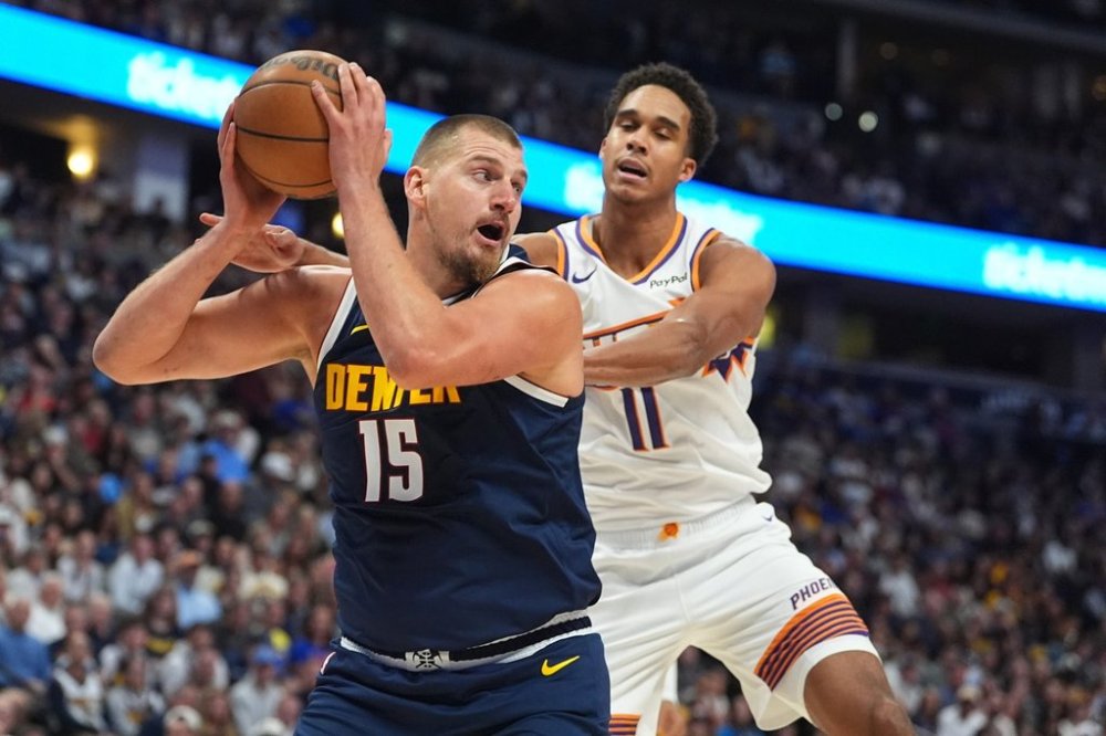 Denver Nuggets center Nikola Jokic, left, pulls in a rebound as Phoenix Suns forward Oso Ighodaro, right, defends in the first half of an NBA basketball game Saturday, Oct. 25, 2025, in Denver. (AP Photo/David Zalubowski)