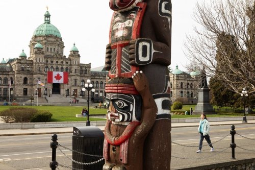 A gigantic Canadian flag hangs over the ceremonial entrance at the legislature as people walk about in Victoria, B.C., on Friday, March 7, 2025. The Greater Vancouver Harbour Authority says the Kwakiutl Bear Pole pole that has stood between the ocean and British Columbia's Parliament buildings since 1966 will be returned to the family of the artist due to its deterioration. THE CANADIAN PRESS/Chad Hipolito