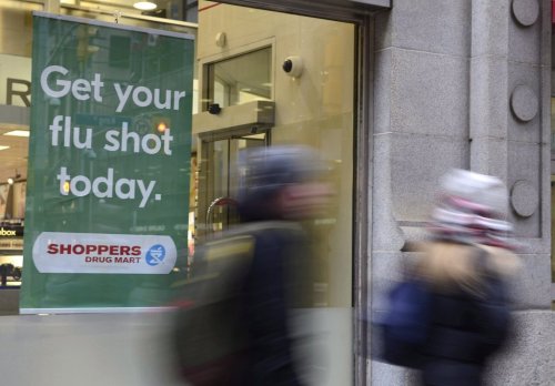 People walk by a sign for flu shots, in Toronto, on Jan. 9, 2018. THE CANADIAN PRESS/Doug Ives