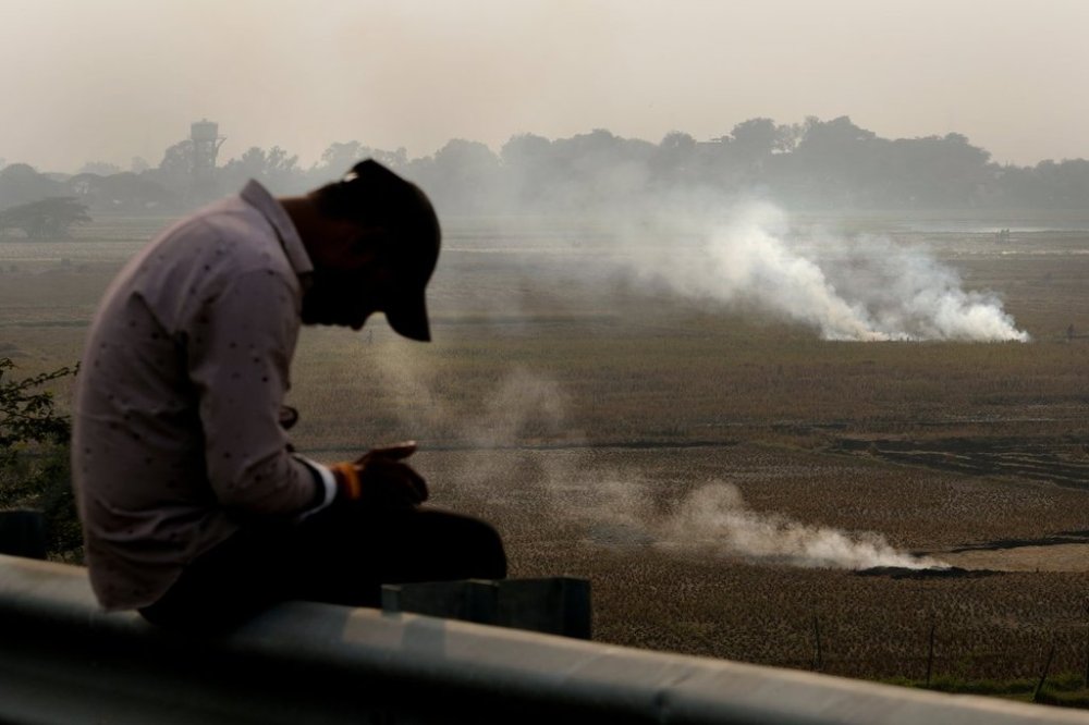 FILE - A person checks his mobile phone as farmers burn crop residue after harvest near Bundelkhand expressway in India, on Nov. 17, 2024. (AP Photo/Manish Swarup, File)