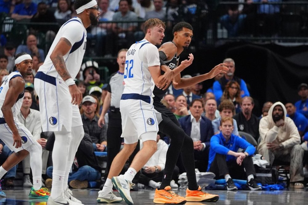 San Antonio Spurs forward Victor Wembanyama, right, is defended by Dallas Mavericks forward Cooper Flagg (32) as forward Anthony Davis, second from left, looks on during the second half of an NBA basketball game in Dallas, Wednesday, Oct. 22, 2025. (AP Photo/LM Otero)
