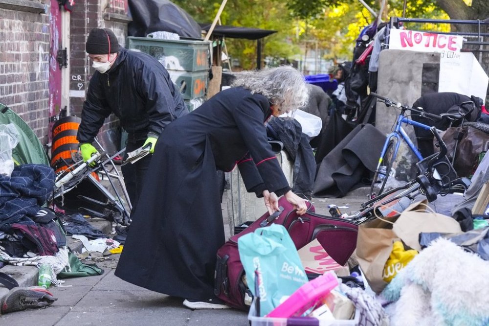 Rev. Canon Maggie Helwig, centre, helps move a resident's belongings as Toronto city workers prepare to clear the encampment at St. Stephen-in-the-Fields Church, in Toronto, on Thursday, Oct. 16, 2025. THE CANADIAN PRESS/Chris Young