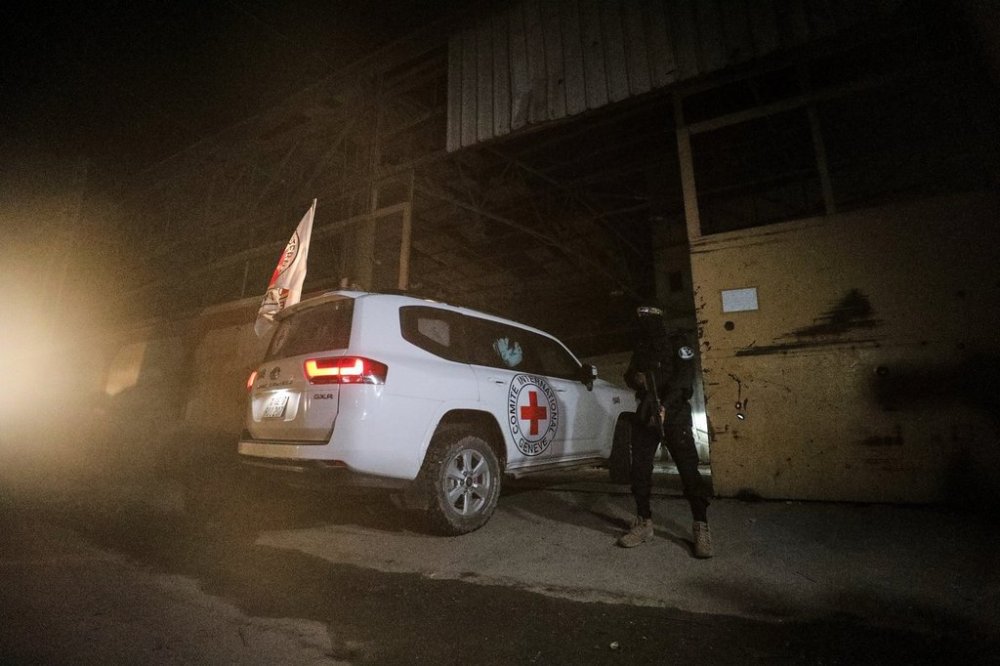 A gunman wearing the uniform of the al-Qassam Brigades, the military wing of Hamas, stands guard as Red Cross vehicles enter a warehouse allegedly to collect coffins containing the bodies of four deceased hostages, in Gaza City, Tuesday, Oct. 14, 2025. (AP Photo/Yousef Al Zanoun)