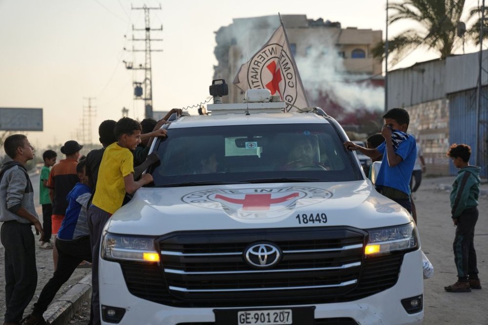 Palestinian kids look into a Red Cross vehicles carrying the bodies of two people believed to be deceased hostages handed over by Hamas make their way toward the Kissufim border crossing with Israel, to be transferred to Israeli authorities, in Deir al-Balah, central Gaza Strip, Thursday, Oct. 30, 2025. (AP Photo/Abdel Kareem Hana)