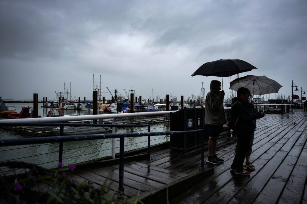 People are silhouetted as they use umbrellas to shield themselves from the rain on the boardwalk overlooking the Steveston Fisherman's Wharf, in Richmond, B.C., on Monday, July 24, 2023. THE CANADIAN PRESS/Darryl Dyck